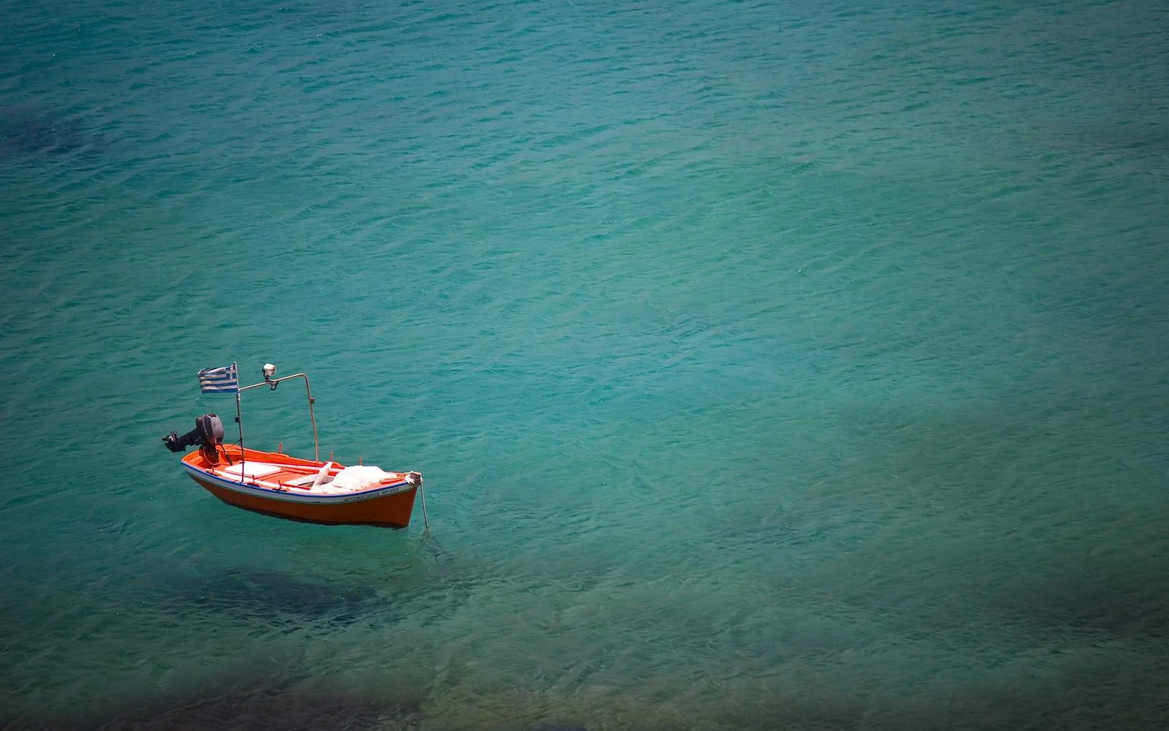 Petite barque rouge au drapeau grec, ancrée sur une eau turquoise
