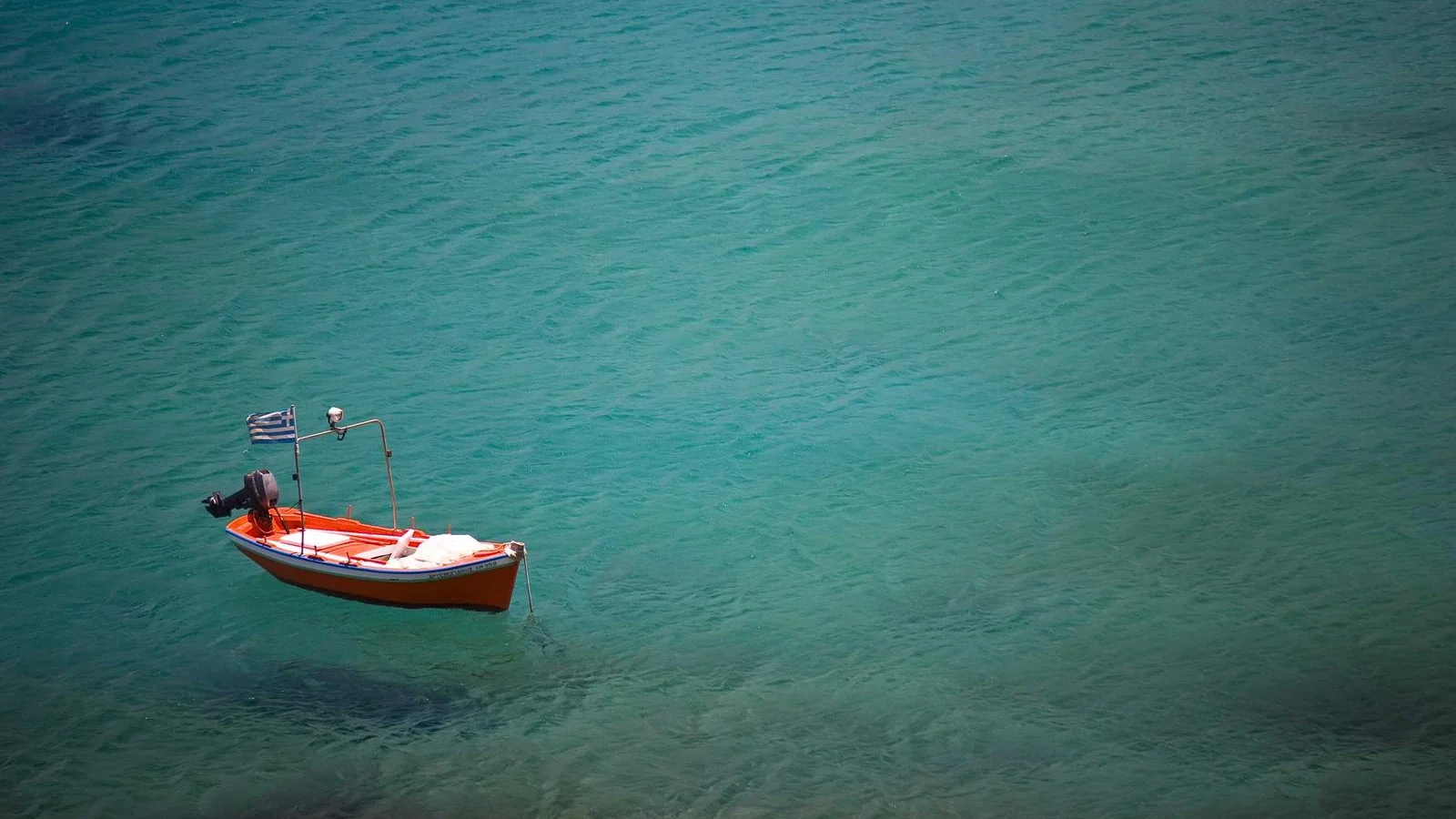Petite barque rouge au drapeau grec, ancrée sur une eau turquoise