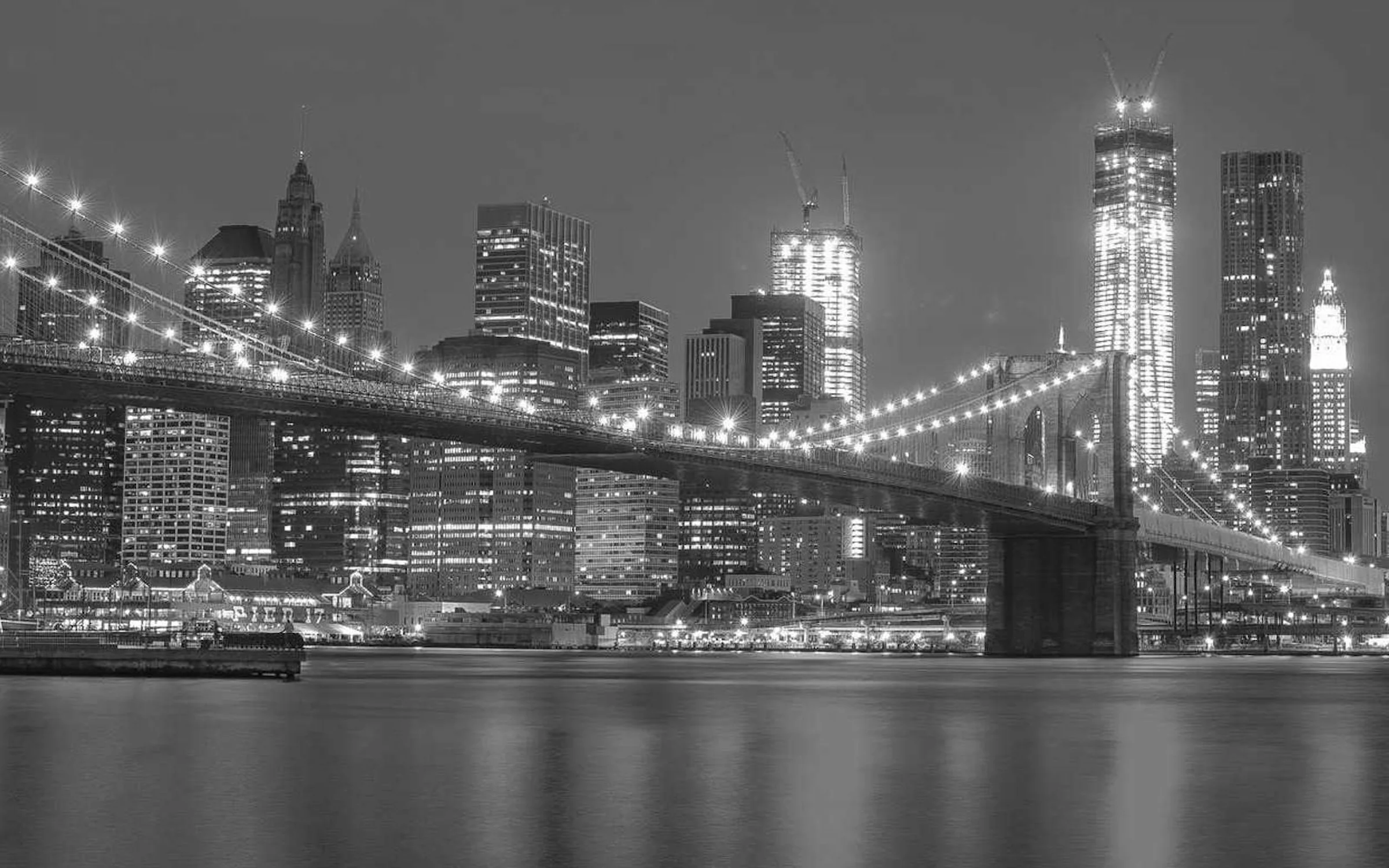 Le pont de Brooklyn illuminé la nuit devant les gratte-ciel de Manhattan, en noir et blanc