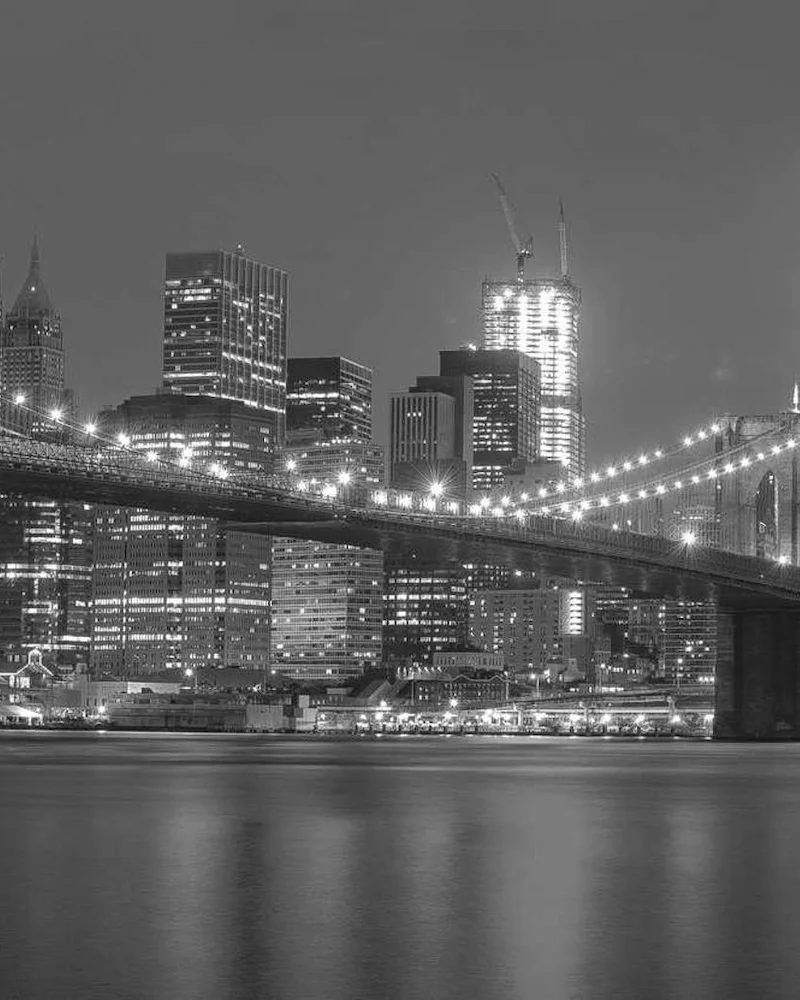 Le pont de Brooklyn illuminé la nuit devant les gratte-ciel de Manhattan, en noir et blanc