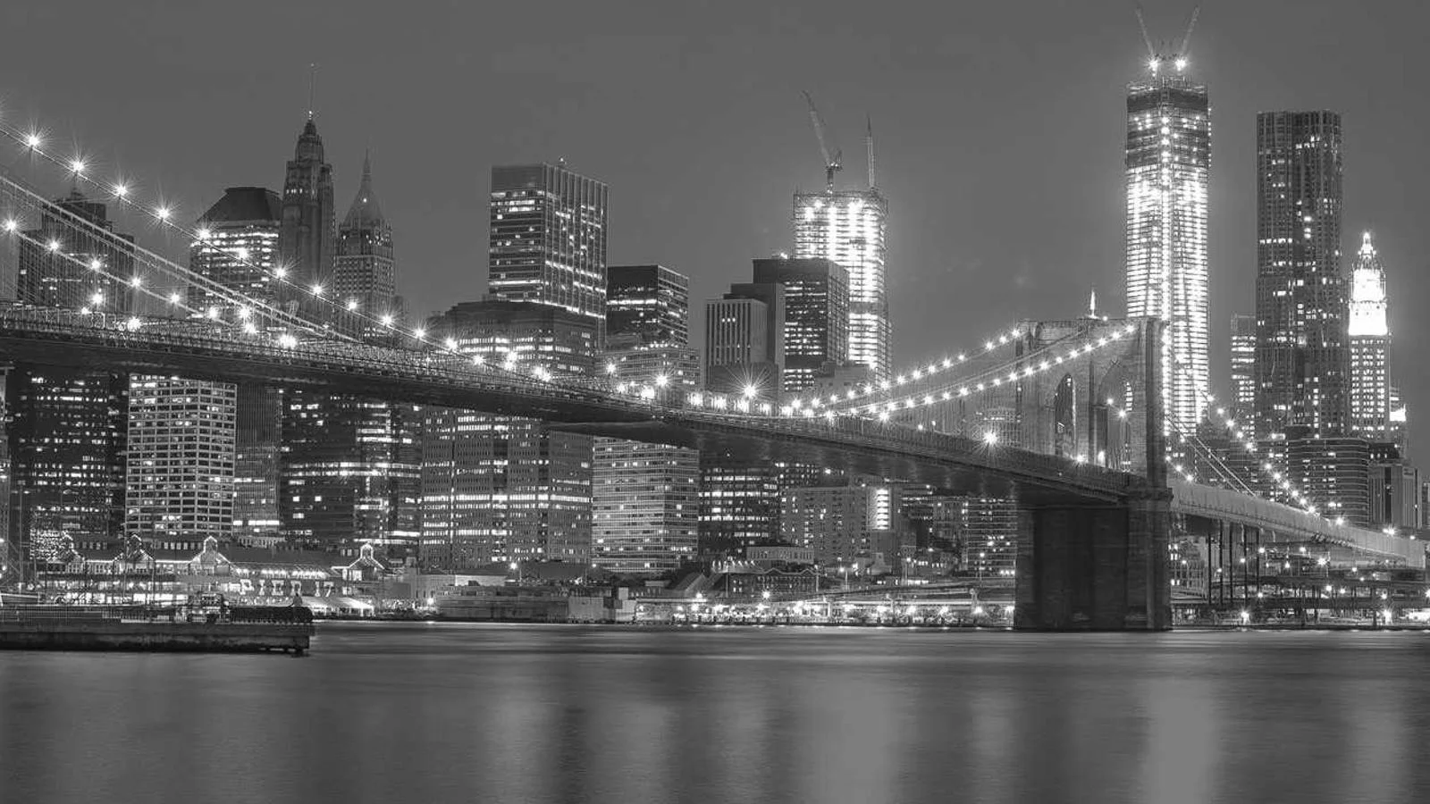 Le pont de Brooklyn illuminé la nuit devant les gratte-ciel de Manhattan, en noir et blanc