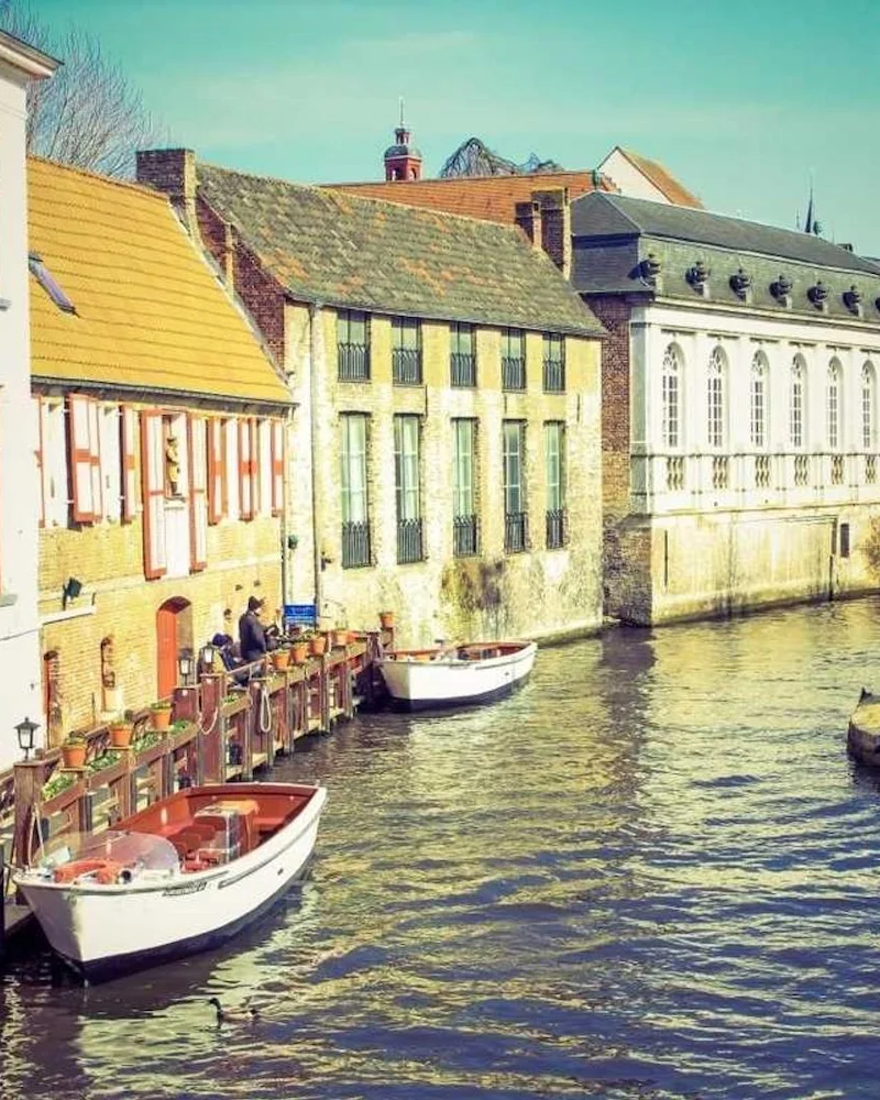 Canal de Bruges bordé de façades anciennes, barques blanches amarrées au quai