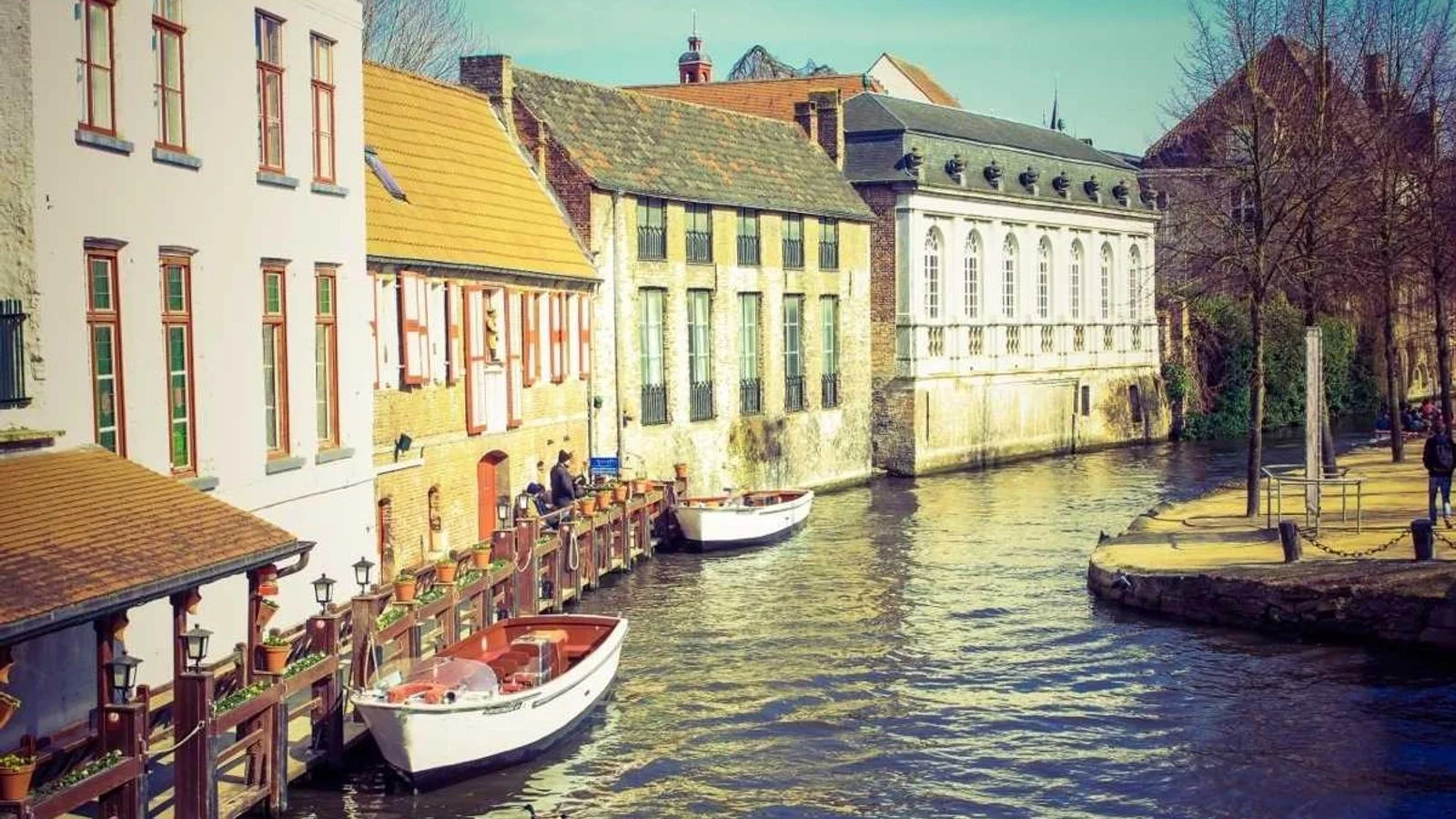 Canal de Bruges bordé de façades anciennes, barques blanches amarrées au quai