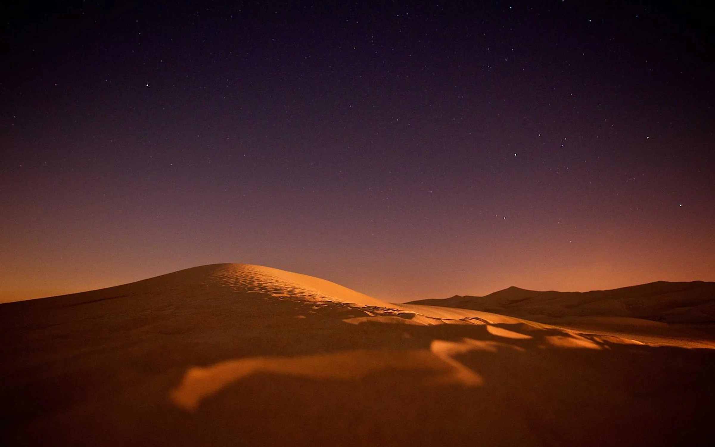 Crête d'une dune orangée sous un ciel étoilé, dans le désert marocain