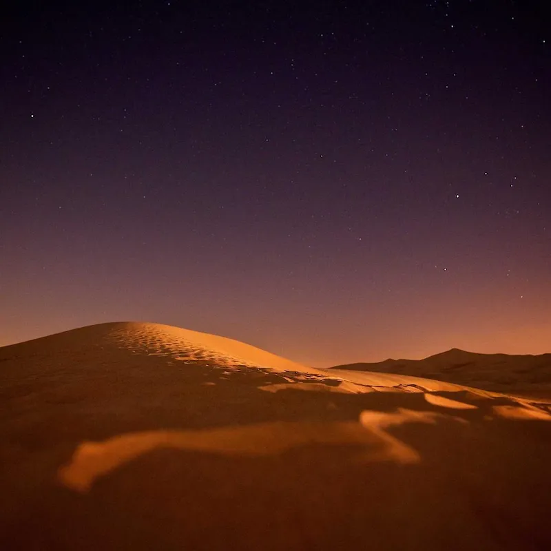 Crête d'une dune orangée sous un ciel étoilé, dans le désert marocain