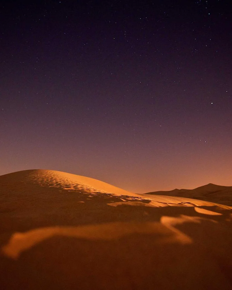 Crête d'une dune orangée sous un ciel étoilé, dans le désert marocain