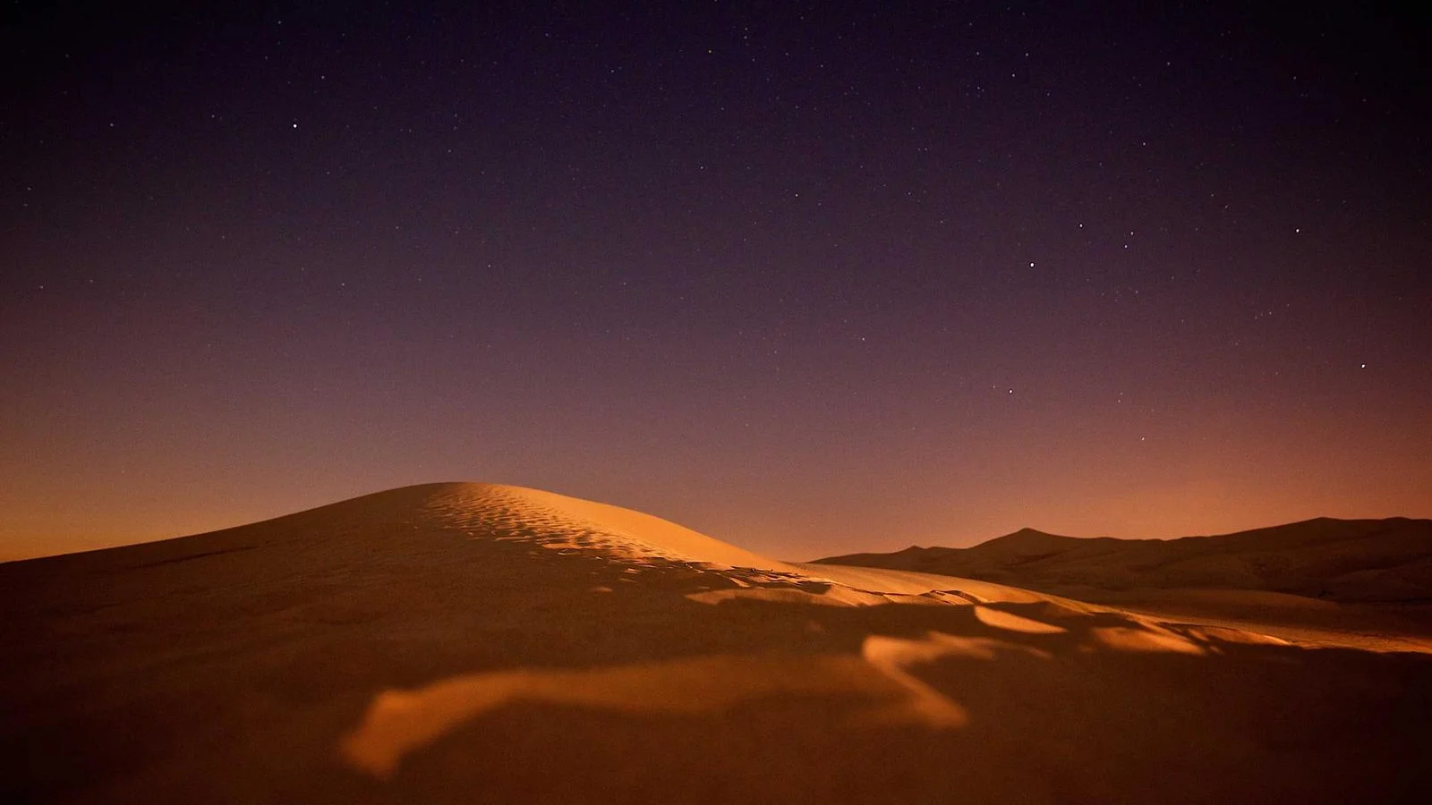 Crête d'une dune orangée sous un ciel étoilé, dans le désert marocain